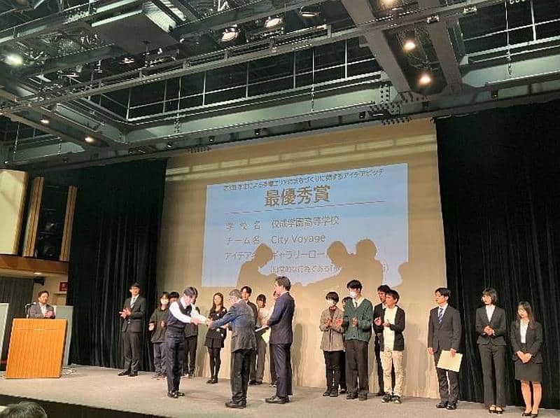 京王電鉄株式会社と独立行政法人都市再生機構(UR)の東日本賃貸住宅本部が開催する「第3回 学生による多摩エリアのまちづくりに関するアイデアピッチ」の表彰式で最優秀賞が表彰されているシーン