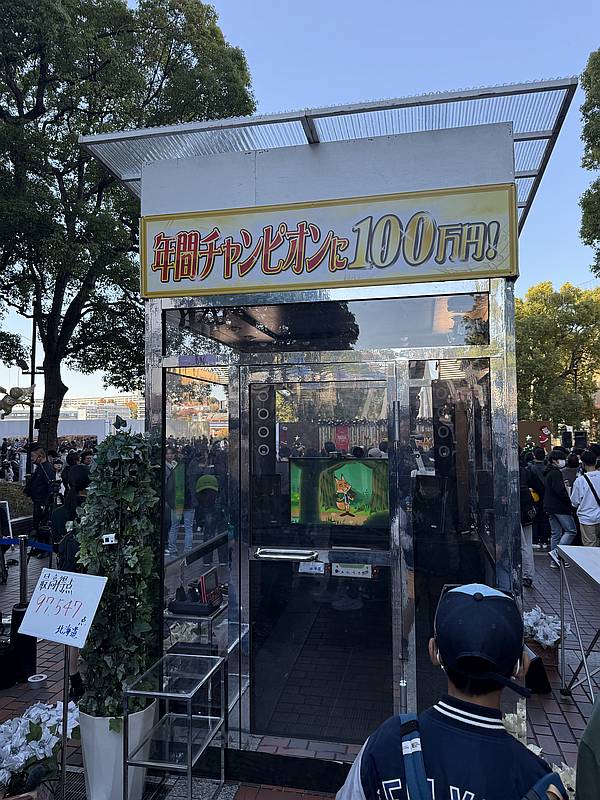 2025年11月22日の透明カラオケの多摩センターでの公開収録のために設置された透明カラオケボックスと北海道王者の特典が掲示