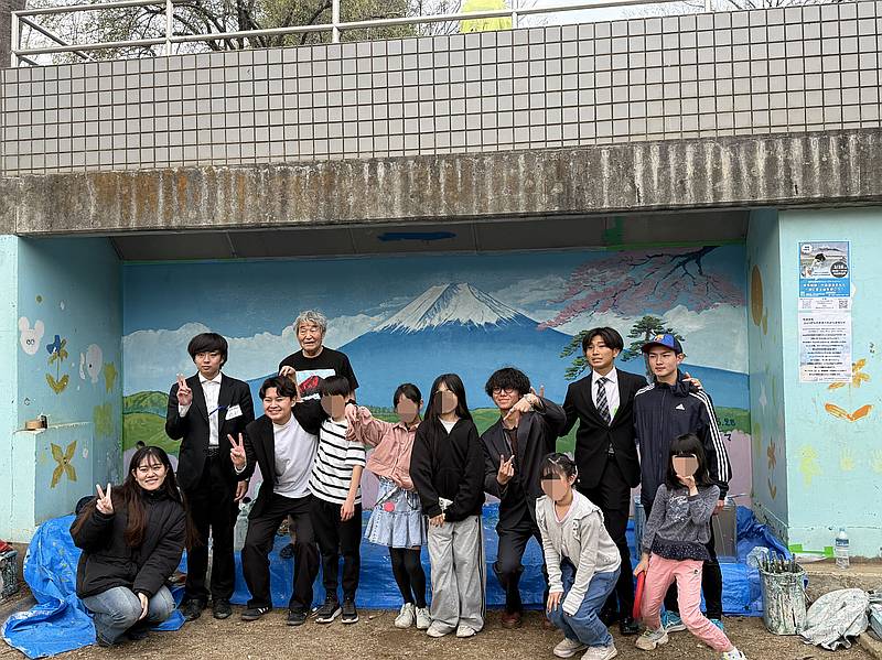 2026年3月28日(土)に南大沢3丁目の溜池公園で「溜池公園壁画リニューアルイベント」でできあがったばかりの桜の咲いた富士山の壁画を背景にして、子どもたちや学生団体Bloomy、銭湯絵師の中島盛夫さん含めた参加者全員での記念撮影