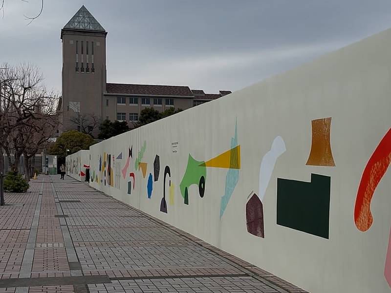 三井アウトレットパーク多摩南大沢のB街区の工事壁は「COUCOUCOU! MINAMIOSAWA」というデザインタイトルで南大沢でお馴染みの東京都立大学のシステムデザイン学部、インダストリアルアート学科のヴィジュアルコミュニケーションデザインスタジオが製作し、2026年3月に設置