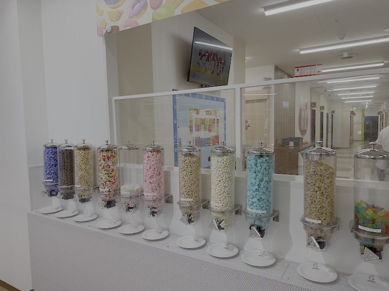 カラオケまねきねこ南大沢店の「おかしバー」のスペースに設置されたラムネやチョコ、グミなどが食べ放題のお菓子サーバー