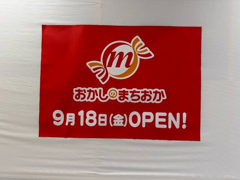 赤地に店舗ロゴと「9月18日(金)OPEN!」が記されたおかしのまちおかのオープン告知ポスター