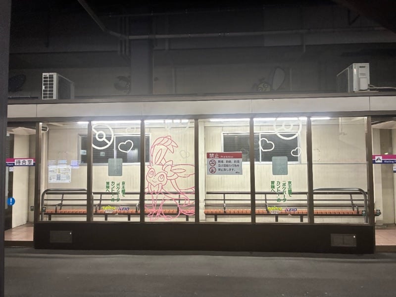 南大沢駅1・2番線ホーム待合室の正面。3枚のガラスのうち中央にピンクのニンフィア線画があり、左右にはハートとモンスターボール、縦書きで京王線でポケパーク カントーの冒険へという文言がある