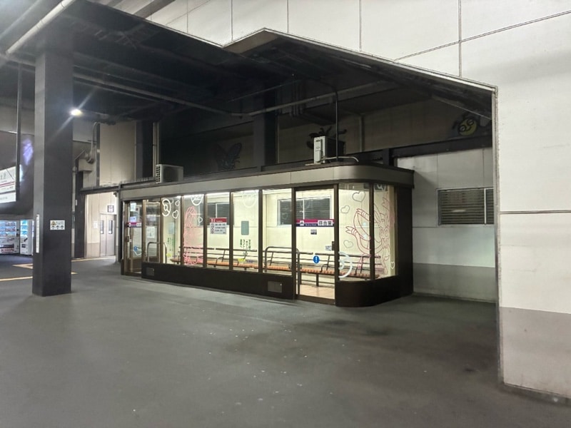 南大沢駅ホーム待合室を角から見た様子。ガラス面にハートとニンフィアの線画があり、内部には木製座面のベンチが置かれている