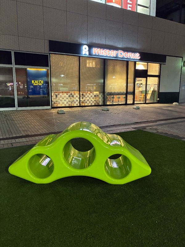 ミスタードーナツ南大沢店前の人工芝。3つの円孔が開いた黄緑色のトンネル状遊具が置かれている