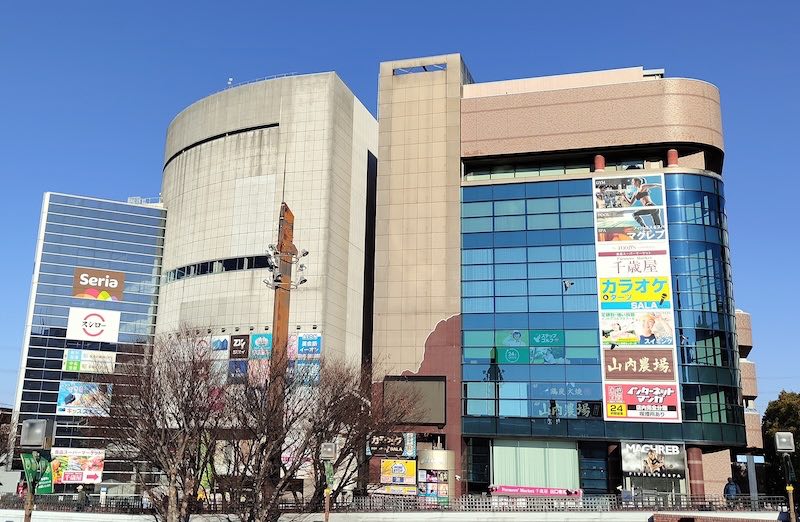 多摩センター駅前のマグレブビルの外観。青いガラス張りの壁面に千歳屋、カラオケ、山内農場、自遊空間の看板が縦に並ぶ