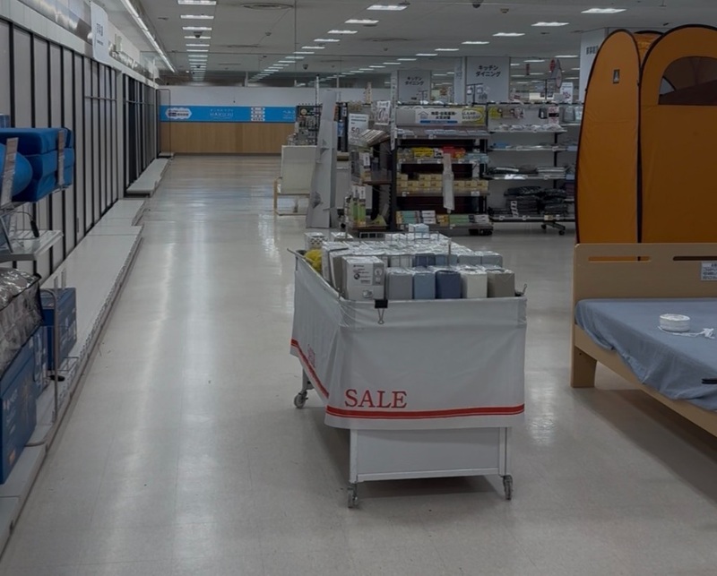 空き棚が続く売り場と、SALEと書かれたワゴン、寝具