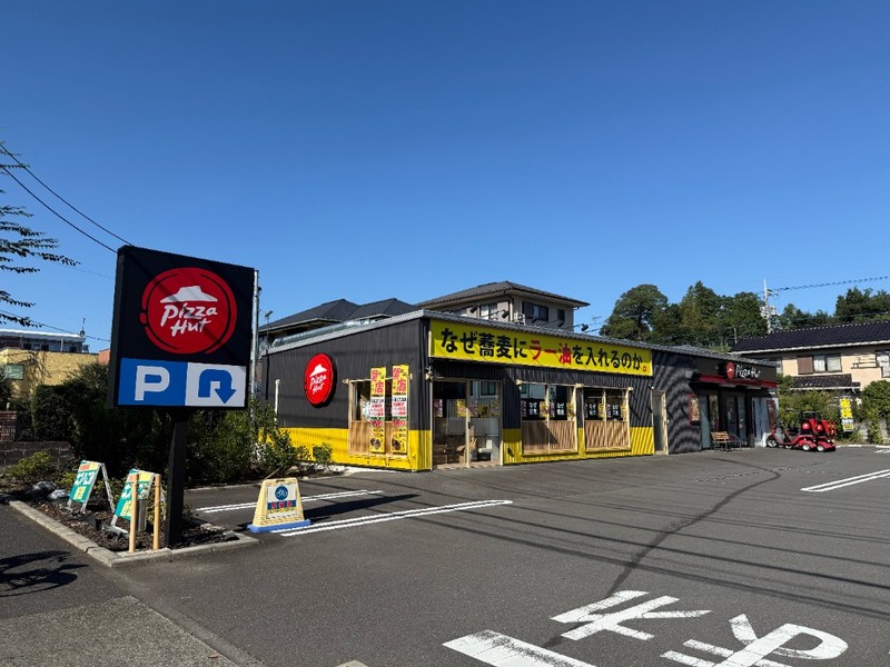ピザハットの看板と共用駐車場の奥にある、黄色い看板のなぜ蕎麦にラー油を入れるのか。八王子野猿街道店とピザハット八王子由木店の建物