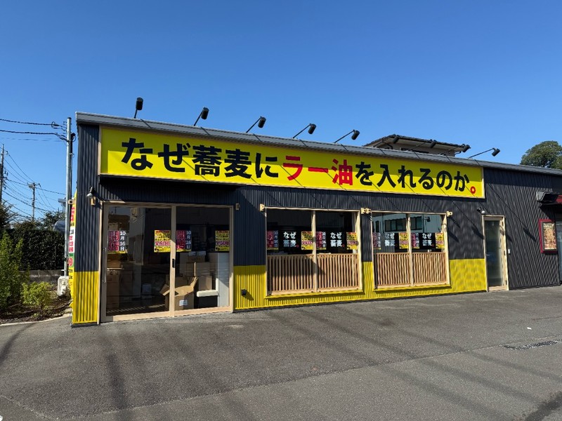 黄色地に「なぜ蕎麦にラー油を入れるのか。」と書かれた大きな看板と、開店10月16日の貼り紙が並ぶ窓
